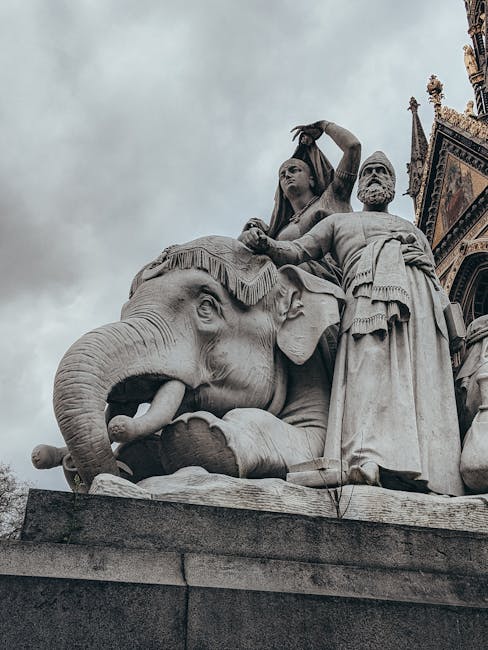 A detailed view of a large stone sculpture situated outdoors in front of the Royal Albert Hall, featuring an elephant with its trunk raised, alongside several human figures in classical attire. The sculpture displays intricate carvings on the figures' clothing and the elephant's textured skin. The surface of the sculpture appears clean and well-maintained, with no visible dirt or grime, suggesting recent or regular cleaning and care. The lighting is natural and slightly overcast, enhancing the stone's subtle color variations. This monument exemplifies outdoor surface cleaning and preservation efforts, possibly supported by companies like westkensingtoncarpetcleaning.co.uk that specialise in meticulous maintenance and sanitisation of historical public artworks and decorative stone surfaces.