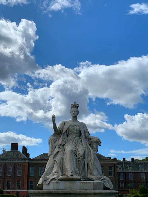 A large stone statue of a regal female figure wearing a crown and flowing garments, seated on a throne with one hand raised in a gesture. The statue is positioned outdoors against a backdrop of a partly cloudy blue sky, with historic brick buildings visible in the background. The scene is well-lit with natural sunlight, highlighting the detailed carvings and smooth surface of the sculpture, which appears clean and well-maintained. This outdoor setting portrays a classical figure likely representing a historical or mythological character, surrounded by an open, urban environment. No cleaning tools or specific surfaces are visible in this image, and it appears to be a peaceful, outdoor commemorative monument.